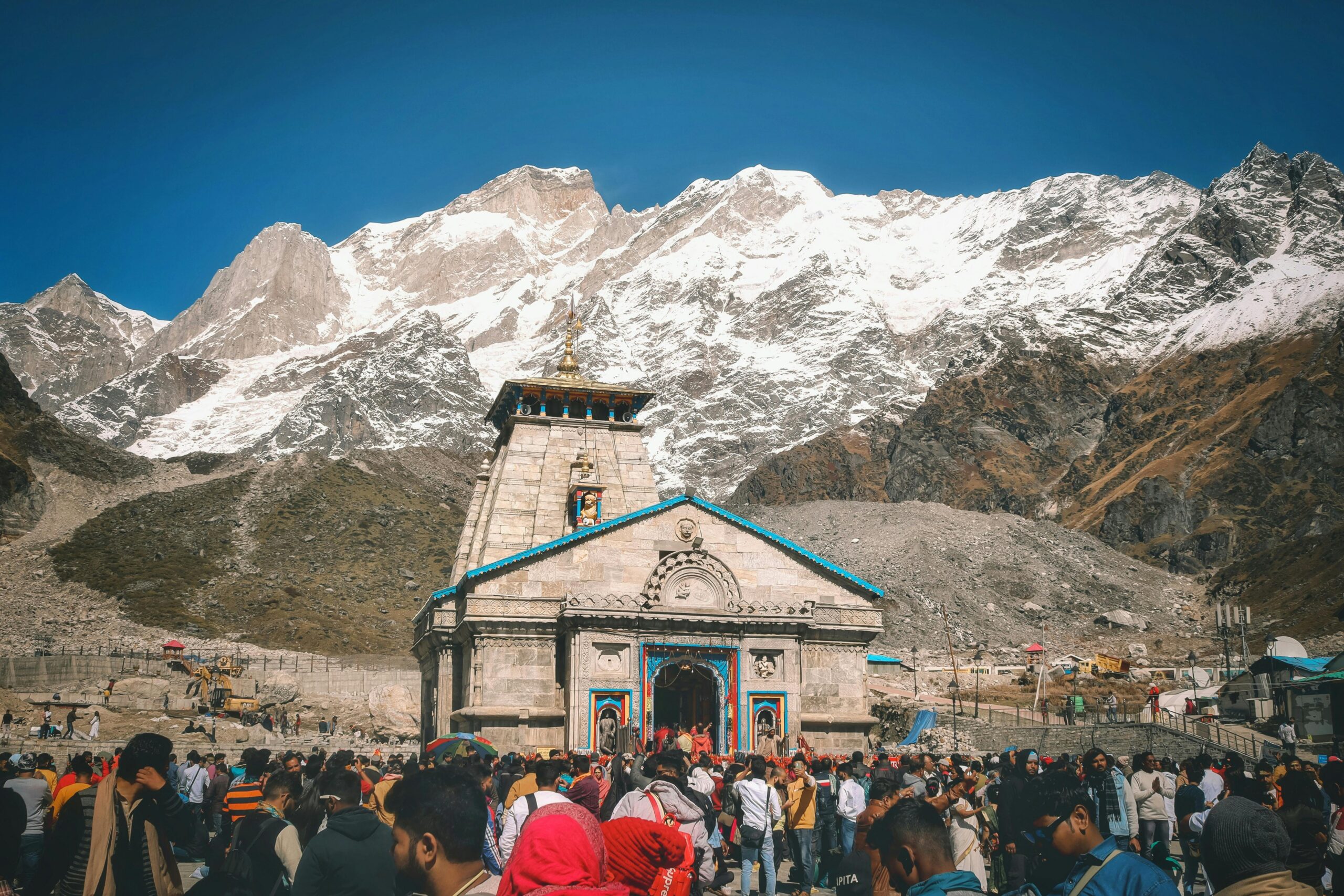 Home A crowd of pilgrims at Kedarnath Temple with snowcapped Himalayan peaks in the background.