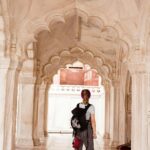 A woman explores the ornate marble hallway of Amber Palace in India, capturing architectural beauty.