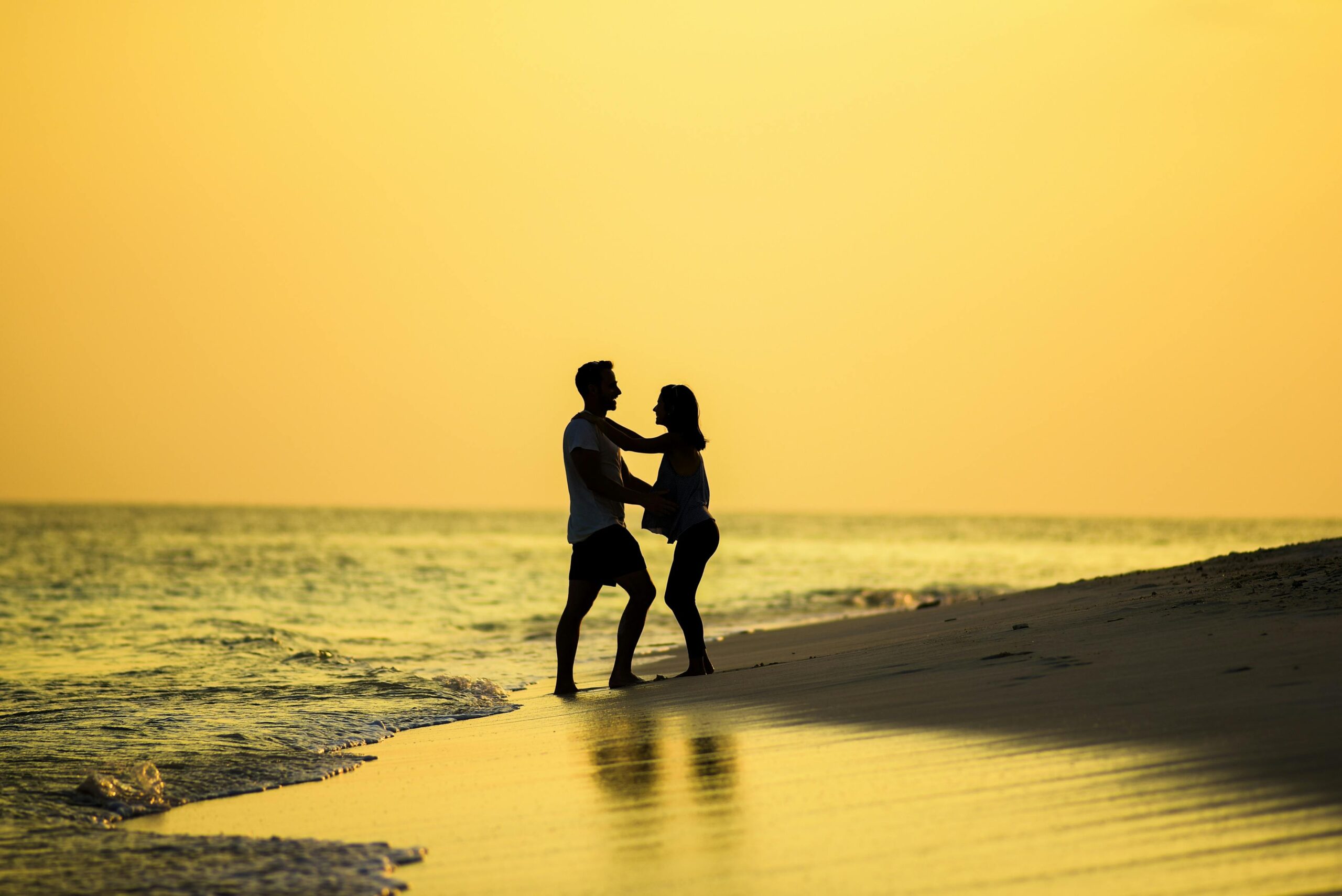 Home Silhouette of a couple embracing on a beach at sunset, capturing a romantic and serene moment.
